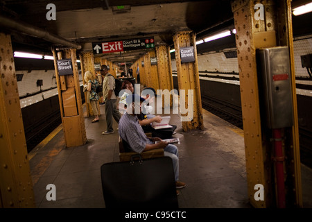 Les gens s'asseoir sur un banc en attendant le métro pour arriver le 15 juin 2010 à Brooklyn, New York. Banque D'Images