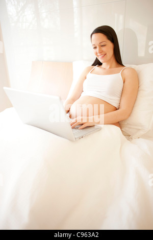 Femme enceinte à l'aide d'un ordinateur portable dans le lit. Banque D'Images