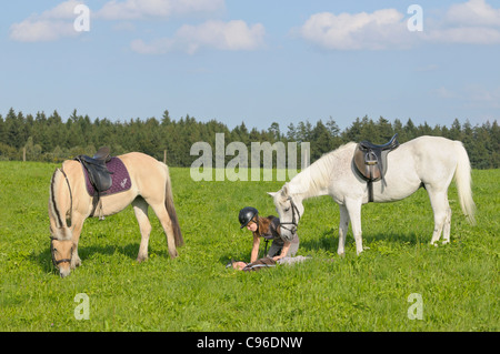 Jeune couchée dans un pré après avoir chuté de son poney, un deuxième avenant prenant soin de sa situation (mise en scène !) Banque D'Images