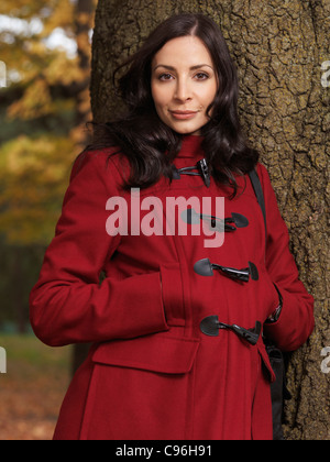 Portrait d'une belle femme en robe rouge à la mode appuyé contre un arbre Banque D'Images