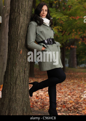 À la mode pour l'automne, la belle jeune femme portant un manteau vert, appuyé contre un arbre dans le parc de l'érable Banque D'Images