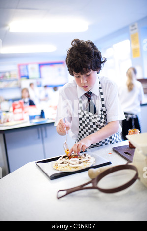 Les enfants de l'école secondaire - un adolescent dans l'avant-plan - dans une classe de cuisine cuisine technologie alimentaire, le Pays de Galles UK Banque D'Images