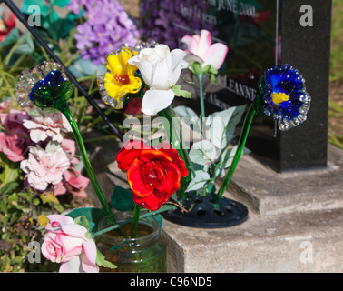 Détail de verre colorées et de fleurs de soie à côté d'une pierre tombale sur une tombe. Cimetière. Banque D'Images