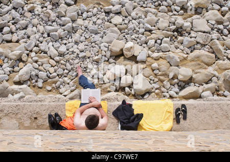 Un homme lit un livre sur le bord de la plage de Camp de Mar, à proximité de Port D'Andratx à Majorque dans les îles Baléares Banque D'Images