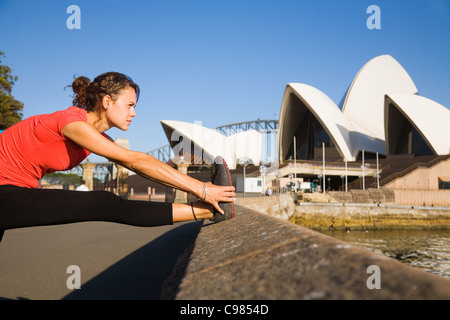 Woman stretching sur Sydney Opera House au bord de l'eau avec en arrière-plan. Sydney, New South Wales, Australia Banque D'Images