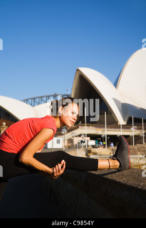 Woman stretching sur Sydney Opera House au bord de l'eau avec en arrière-plan. Sydney, New South Wales, Australia Banque D'Images