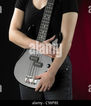 Détail d'une femme et d'un black bass guitare devant de dos rougeâtre en partie Banque D'Images