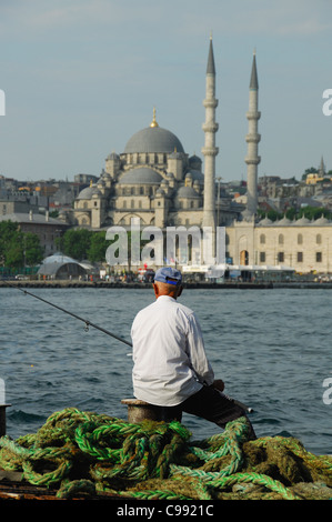 ISTANBUL, TURQUIE. Un homme âgé de la pêche dans la Corne d'or à Karakoy, avec la Mosquée de Yeni derrière d'Eminonu. 2011. Banque D'Images