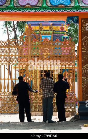 Trois hommes debout indiennes à l'extérieur des portes d'un village temple hindou. L'Andhra Pradesh, Inde Banque D'Images