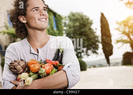 Italie, Toscane, Magliano, Young man holding variété de légumes, smiling Banque D'Images