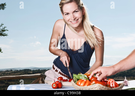 Italie, Toscane, Magliano, jeune homme debout près de la table et coupe femme tomates, smiling Banque D'Images