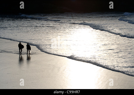 Deux surfeurs de marcher le long du bord de l'eau, la baie de Treyarnon, Cornwall, England, UK Banque D'Images