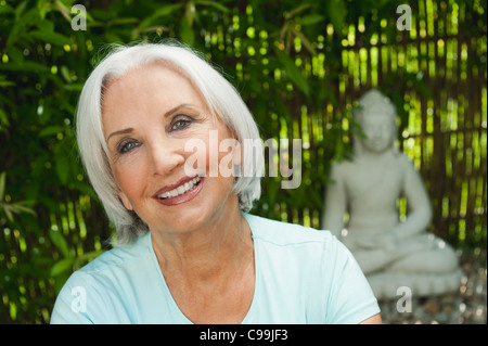 Germany, Bavaria, Senior woman smiling with Buddha statue in background Banque D'Images