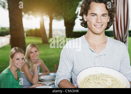 Italie, Toscane, Magliano, Young man holding bol de pâtes et les femmes en arrière-plan, smiling Banque D'Images