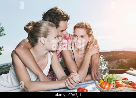 Italie, Toscane, Magliano, jeune homme et femmes embrassant près de table, smiling Banque D'Images