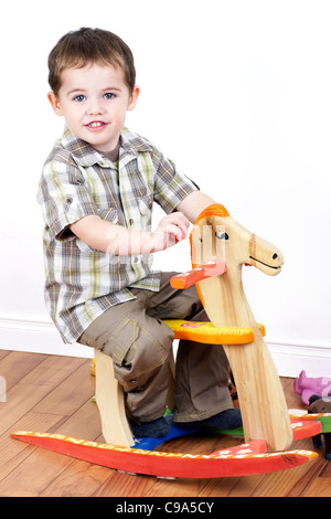 Cute little boy riding a handcrarfted cheval à bascule en bois, chaise, studio shot verticale. Banque D'Images