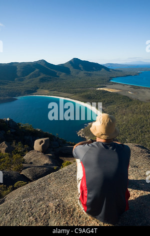 Un homme donne sur Wineglass Bay à partir du sommet du mont Amos. Parc national de Freycinet, Tasmanie, Australie Banque D'Images