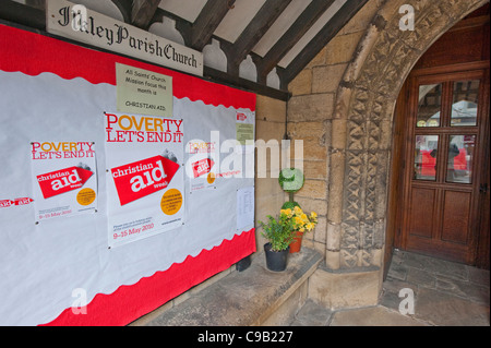 À l'intérieur de porche de l'église (Christian Aid affiches sur la carte affichage, porte en bois, arche sculptée en pierre) - All Saints' Church, Bradford, Yorkshire, Angleterre, Royaume-Uni. Banque D'Images