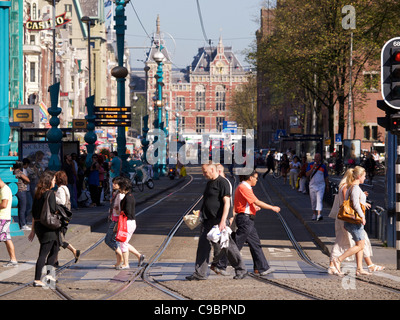 Les personnes qui traversent la rue Damrak avec la gare centrale d'Amsterdam en arrière-plan, les Pays-Bas Banque D'Images