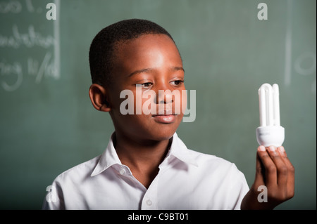 Boy holding energy saving lightbulb en classe, Johannesburg, la Province de Gauteng, Afrique du Sud Banque D'Images