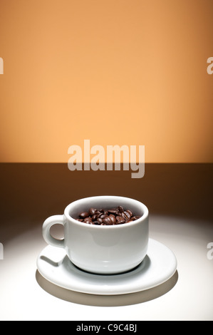 Tasse de café remplie de grains de café, fond orange Banque D'Images