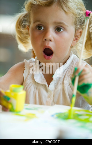 Petite fille peinture avec expression surpris sur le visage Banque D'Images