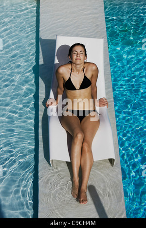 Jeune femme en train de bronzer sur une chaise longue à la piscine Banque D'Images