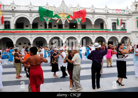 Le Mexique, Veracruz, des couples dansant dans le Zocalo avec façade d'immeubles gouvernementaux derrière ornés de décorations lumineuses Banque D'Images