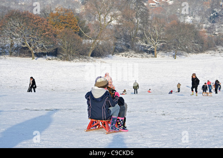 Les enfants de la luge sur la neige a couvert la colline du Parlement, Hampstead Heath, Londres, Angleterre. Banque D'Images