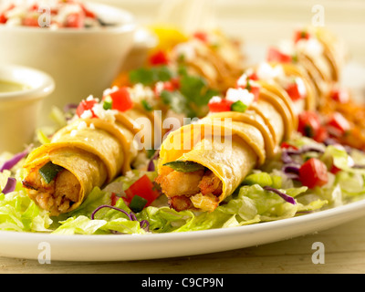 Deux chicken taquitos garnie de sauce, de salsa et de fromage servi sur un lit de laitue avec haricots noirs et riz Banque D'Images