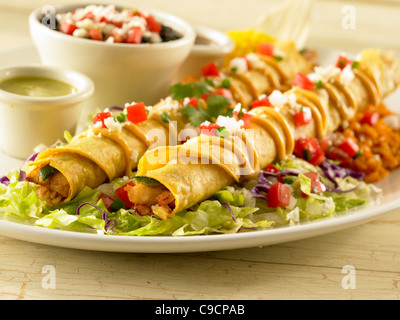 Deux chicken taquitos garnie de sauce, de la salsa et du fromage et servi sur un lit de laitue avec haricots noirs et riz Banque D'Images