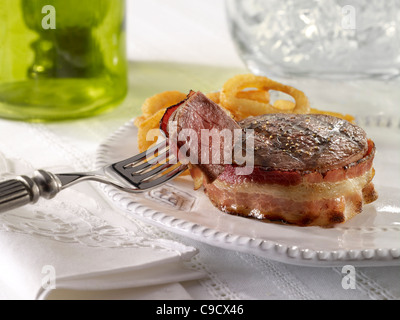 Filet de boeuf enrobé de bacon et servi avec des rondelles d'oignon Banque D'Images