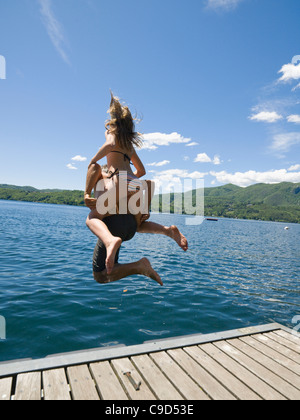 L'Italie, Piémont, vue arrière du père et fille (14-15) de sauter du quai en bois dans le lac d'Orta Banque D'Images