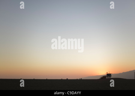 Coucher du soleil sur la plage de Santa Monica. Un sauveteur tour et un petit troupeau d'oiseaux silhouette sur le soleil couchant. Banque D'Images