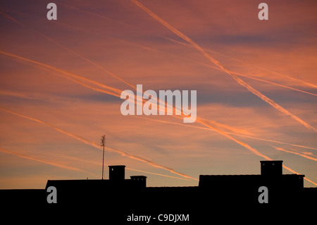 Silhouettes de toit de ciel coucher contre des traînées de vapeur et d'avion Banque D'Images