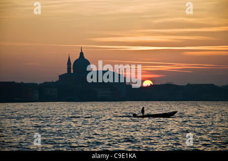 Canal Giudecca, Venise, Italie. Un homme dans un bateau se déplace de l'autre côté du canal alors que le soleil se couche sur Chiesa del Redentore, une église sur l'île de la Giudecca Banque D'Images