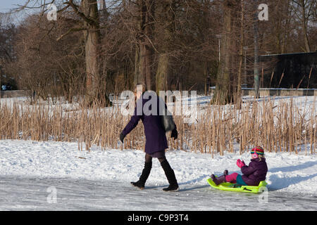 Grand gel : femme tirant un enfant sur un sledg, parmi les gens de patinage de glace dans le Vondelpark, Amsterdam, février 2012. La nuit d'aussi bas que -18 a quitté les villes canaux et d'étangs gelés - et les Néerlandais ne perdez pas l'occasion d'enfiler leurs patins à glace. Banque D'Images