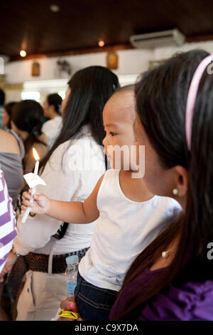 Lapu-Lapu City, Philippines, 26/02/2012 : 200 à 300 bébés baptisés dans un seul 3 heure cérémonie à Mactan Air Base Chapelle. Garçon tenant une bougie allumée, porté par sa mère. Banque D'Images