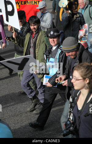 Londres, Royaume-Uni, le 14 mars, 2012 Un agent de liaison aux côtés de manifestants promenades holding a placard qui écrit le mot occupent. La police métropolitaine a déclaré que "l'Équipe de liaison de protestation ont été introduites afin d'améliorer le dialogue et la compréhension entre les manifestants et la police". Banque D'Images