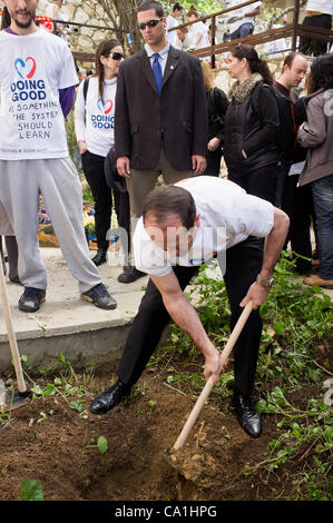 Nir Barkat, maire de houes à planter un arbre dans un jardin communautaire sur la rue Stern à Kiryat Yovel sur 'bonnes actions Day'. Une alerte garde du corps garde un oeil sur le dos du maire. Jérusalem, Israël. 20-Mar-2012. Banque D'Images