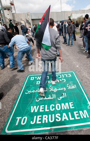 Bethléem, TERRITOIRES PALESTINIENS OCCUPÉS - le 30 mars : un Palestinien holding stones marche sur un écriteau 'Bienvenue à Jérusalem" au cours d'affrontements au checkpoint de Bethléem au cours de la Journée de la Terre de protestation. Banque D'Images