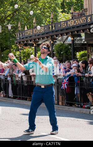 Un jongleur homme divertit la grande foule de gens heureux (de nombreux drapeaux de l'Union Jack) regarder, debout & doublure la route à l'événement du relais de la flamme olympique à Harrogate, Yorkshire, UK. Le mardi 19 juin 2012. Banque D'Images