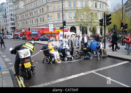 Londres, Royaume-Uni. 18/04/12. Un cycliste moteur hits le manifestant sa chaîne, que les personnes handicapées contre les coupures (ATLC) bloquer la route à Trafalgar Square. La manifestation est de mettre en évidence les coupures aux prestations. Banque D'Images