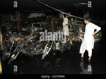 Les gens recherchent des véhicules brûlés et des motos, qui ont pris feu à cause d'une raison inconnue, après l'incendie survenu en sous-sol de terres de l'Ouest Vacances à Bahadurabad zone sur tôt le matin à Karachi le Lundi, Mai 07, 2012. Banque D'Images