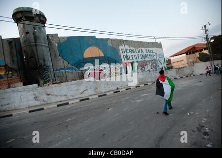 Bethléem, dans les territoires palestiniens - 14 MAI 2012 : un Palestinien portant un drapeau marches au-delà du mur de séparation israélien dans le camp de réfugiés de Aida à la veille du jour de la Nakba, commémorant la 'catastrophe' que les réfugiés palestiniens expulsés de ce qui est devenu l'état moderne d'Israël en 1948. Banque D'Images