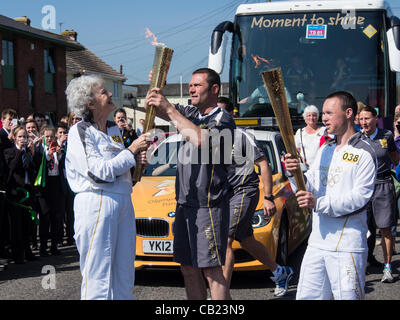 Glastonbury, Somerset, Royaume-Uni, 22 mai 2012. La flamme olympique est passée entre deux porteurs au relais avant le début des Jeux Olympiques de Londres, 2012. Pamela Shaw, 63 ans, est maintenant le flambeau allumé et le transmettre à l'autre coureur. Banque D'Images