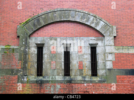 Old weathered moussus et mur de briques avec arche en pierre et fenêtres étroites Banque D'Images
