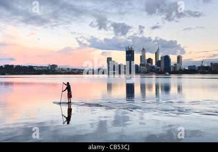 Pagayez surfer sur la rivière au lever du soleil avec l'horizon de la ville au loin. Banque D'Images