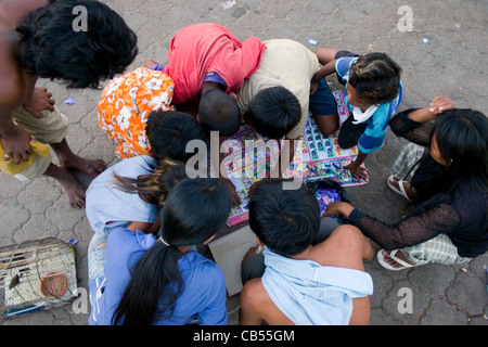 Un groupe d'enfants sont à la recherche à un autocollant coloré collection sur un trottoir de la ville de Phnom Penh, Cambodge. Banque D'Images