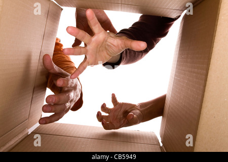 Vue de l'intérieur de boîte en carton avec trois mains en essayant d'atteindre le contenu (selective focus) Banque D'Images